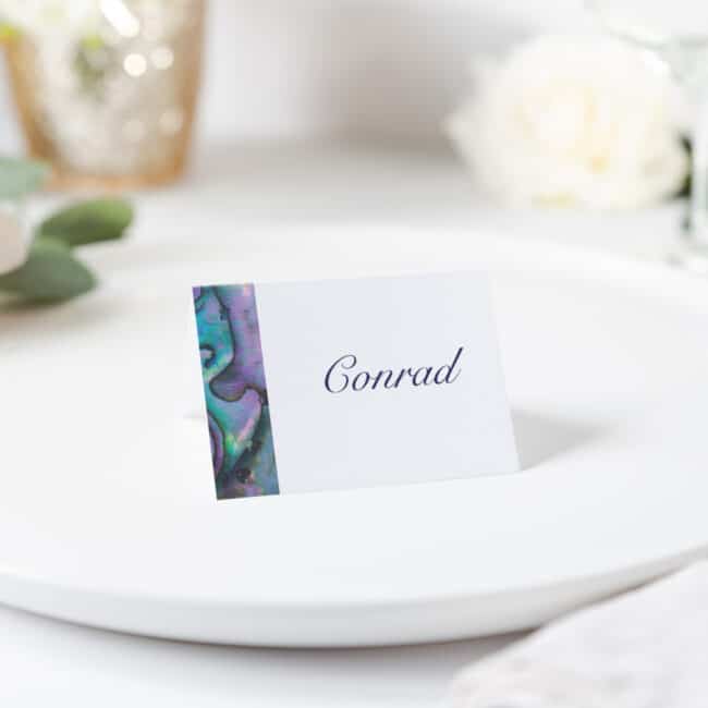 Paua shell printed on white tent card with guest name sitting on plate