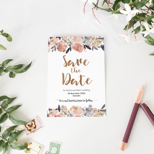 save the date card next to flowers and pen